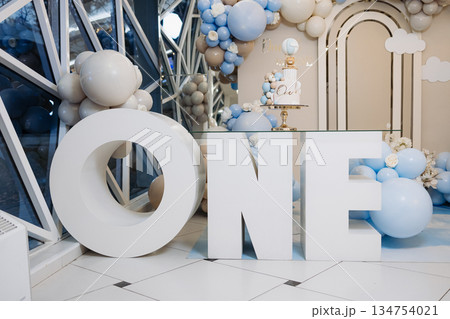 An exquisite and stylish First Birthday decoration featuring grand ONE letters that are beautifully surrounded by a delightful assortment of blue and white balloons, creating a festive atmosphere 134754021