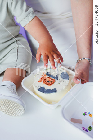 A joyful toddler having fun while enjoying some delicious cake with adult supervision nearby 134754059