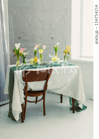 Immerse in a delightful Floral Table Setting for Spring Gatherings, featuring vibrant Fresh Blooms and a Vintage Wooden Chair, adding charm and comfort to elevate your celebration 134754214