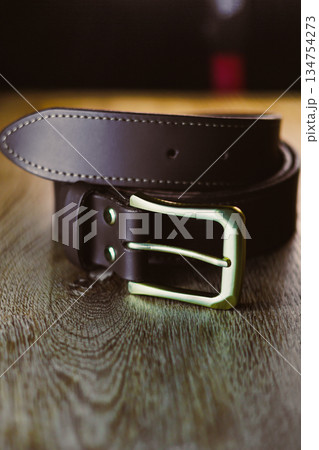 An Elegant Black Leather Belt featuring a Silver Buckle rests on a Wooden Table Surface, showcasing its refined craftsmanship and stylish detailing, perfect for enhancing any sophisticated outfit 134754273