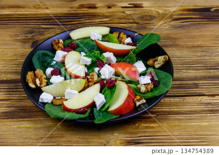 Autumn spinach salad with apple, feta cheese, walnut and dried cranberry on wooden table. Healthy vegetarian food 134754389