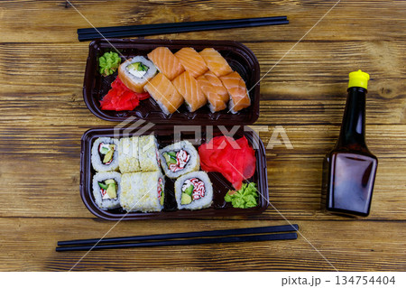 Set of sushi rolls in plastic boxes, soy sauce and chopsticks on wooden table. Top view. Sushi for take away or delivery of sushi in plastic containers Set of sushi rolls in plastic boxes, soy sauce and chopsticks on wooden table. Top view. Sushi for take away or delivery of sushi in plastic containers 134754404