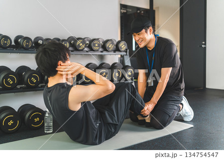 スポーツジムで腹筋・腹斜筋を鍛える・筋トレをする男性と指導するパーソナルトレーナー 134754547