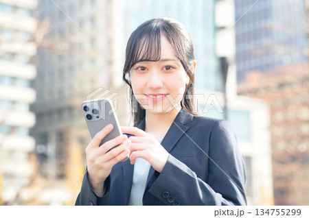 オフィス街でスマホを使用するスーツの女性 オフィス街でスマホを使用するスーツの女性 134755299