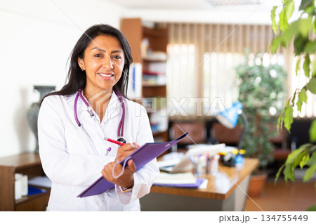 Polite female doctor filling out medical form at clipboard Polite female doctor filling out medical form at clipboard 134755449