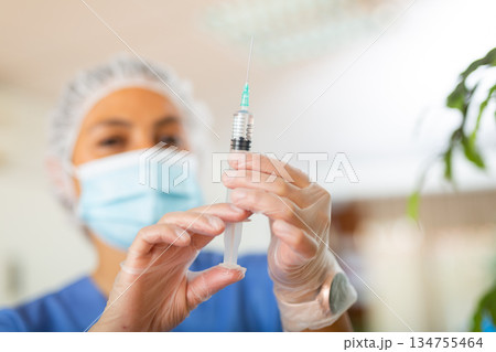 Female nurse in mask holding syringe for injection Female nurse in mask holding syringe for injection 134755464