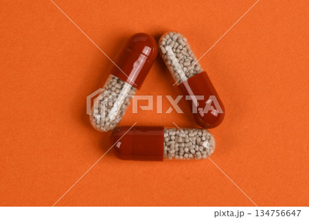 Triangle Arrangement of Three Medical Capsules on Orange Background Triangle Arrangement of Three Medical Capsules on Orange Background 134756647