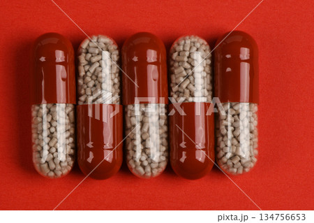Row of Red and Clear Medical Capsules Filled with Pellets on Red Background Row of Red and Clear Medical Capsules Filled with Pellets on Red Background 134756653