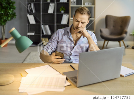 Sad man with stress and anxiety using phone and laptop for overtime work at office 134757785