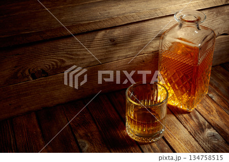 Elegant whiskey glass and decanter on a old wooden table. Elegant whiskey glass and decanter on a old wooden table. 134758515