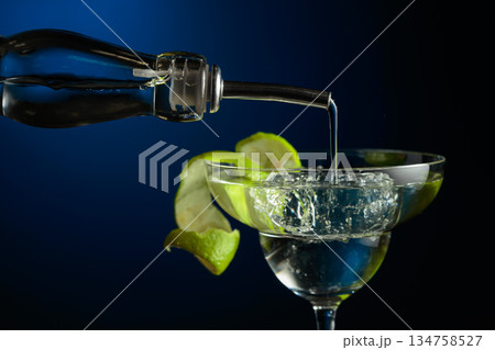 Vodka or gin is poured into a glass with ice. Vodka or gin is poured into a glass with ice. 134758527