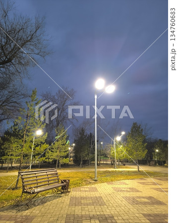 Experience the quiet beauty of an evening park scene. A peaceful moment with a park bench under streetlights, offering a tranquil escape. Ideal for relaxation, urban life, or travel destinations. Experience the quiet beauty of an evening park scene. A peaceful moment with a park bench under streetlights, offering a tranquil escape. Ideal for relaxation, urban life, or travel destinations. 134760683