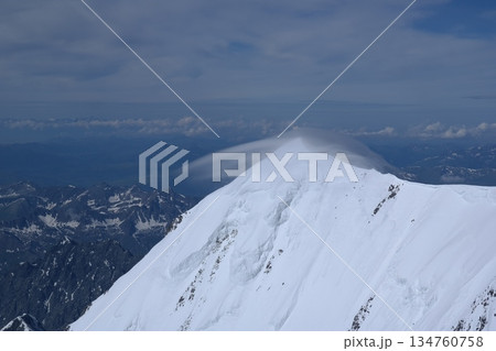 A stunning rock formation covered in snow, set against a clear blue sky with fluffy clouds in the background, creating a peaceful and breathtaking mountain landscape. 134760758