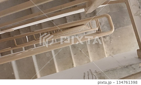 A unique perspective of a modern staircase shaft. The architectural design forms an intriguing geometric pattern, suitable for backgrounds that emphasize depth and descent. A unique perspective of a modern staircase shaft. The architectural design forms an intriguing geometric pattern, suitable for backgrounds that emphasize depth and descent. 134761398