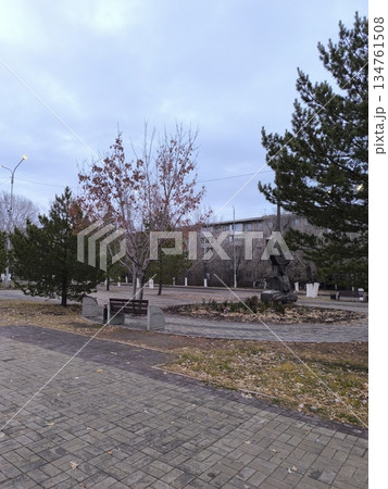 A peaceful city park scene with a paved walkway, benches, and scattered leaves under a cloudy sky. This image captures calmness, ideal for urban planning or landscape design. 134761508