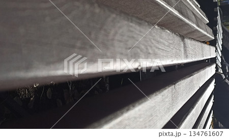 This image features a close-up of a wooden fence, highlighting geometric lines and shadows that create an abstract visual. Perfect for backgrounds and textures in design projects. 134761607