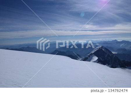 A stunning rock formation covered in snow, set against a clear blue sky with fluffy clouds in the background, creating a peaceful and breathtaking mountain landscape. A stunning rock formation covered in snow, set against a clear blue sky with fluffy clouds in the background, creating a peaceful and breathtaking mountain landscape. 134762474