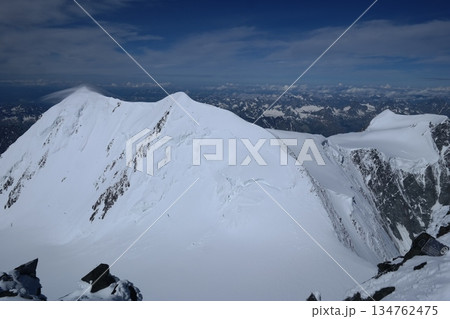A stunning rock formation covered in snow, set against a clear blue sky with fluffy clouds in the background, creating a peaceful and breathtaking mountain landscape. 134762475