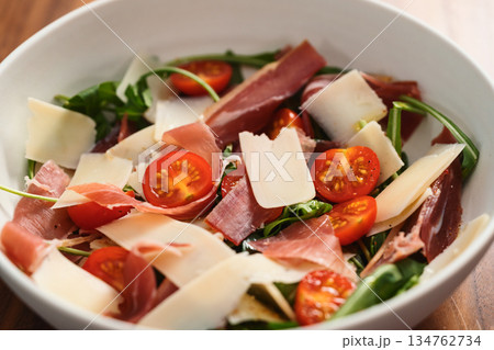 Salad with prosciutto, tomato, arugula leaves and parmesan cheese in white bowl closeup Salad with prosciutto, tomato, arugula leaves and parmesan cheese in white bowl closeup 134762734
