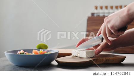 Man cutting feta cheese on olive wood board for greek salad Man cutting feta cheese on olive wood board for greek salad 134762842