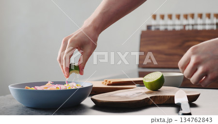 Man squeeze lime into greek salad in blue bowl Man squeeze lime into greek salad in blue bowl 134762843
