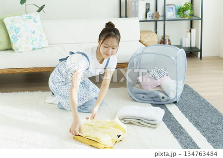 リビングルームで洗濯物を畳む若い女性 リビングルームで洗濯物を畳む若い女性 134763484