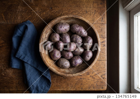Fresh raw purple potatoes in a rustic wooden bowl on an aged table next to a blue linen napkin 134765149