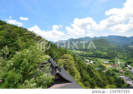 山形県の観光名所である山寺立石寺の伝統的な建築の屋根と背後に広がる新緑の山々 134767393