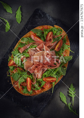 Open-Faced Sandwich with Prosciutto, Arugula and Cherry Tomatoes on Dark Background Open-Faced Sandwich with Prosciutto, Arugula and Cherry Tomatoes on Dark Background 134767975