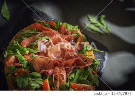 Open-Faced Sandwich with Prosciutto, Arugula and Cherry Tomatoes on Dark Background Open-Faced Sandwich with Prosciutto, Arugula and Cherry Tomatoes on Dark Background 134767977