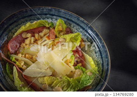 Gourmet Caesar salad with crispy bacon, parmesan shavings and croutons in a blue bowl, top view 134769280