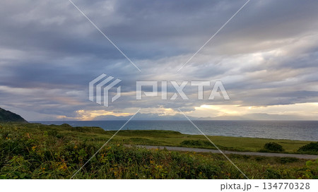 Evening coastal view on the Kuril Islands. Rolling green hills meet the sea under a dramatic sky. Sunlight streams through the clouds Evening coastal view on the Kuril Islands. Rolling green hills meet the sea under a dramatic sky. Sunlight streams through the clouds 134770328