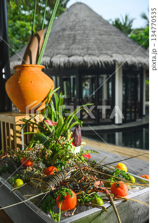 Fresh spiny lobsters on ice at a seafood market with tropical greenery and tomatoes Fresh spiny lobsters on ice at a seafood market with tropical greenery and tomatoes 134770535