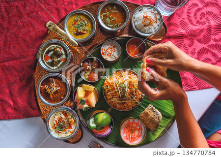 Woman's hand dipping naan bread into traditional Indian curry on a diverse Thali platter Woman's hand dipping naan bread into traditional Indian curry on a diverse Thali platter 134770784
