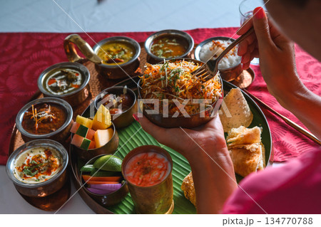 Woman's hand dipping naan bread into traditional Indian curry on a diverse Thali platter Woman's hand dipping naan bread into traditional Indian curry on a diverse Thali platter 134770788