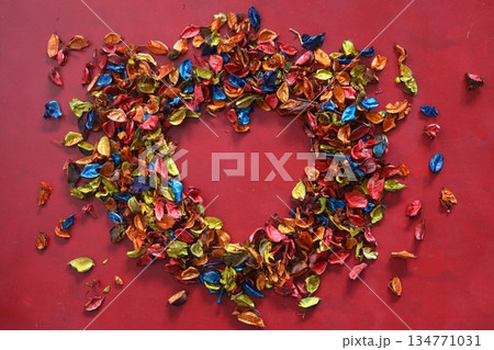 A heart of multicolored, dried rose petals on a burgundy background. Valentines Day card, March 8, Mothers Day. Top view.. 134771031