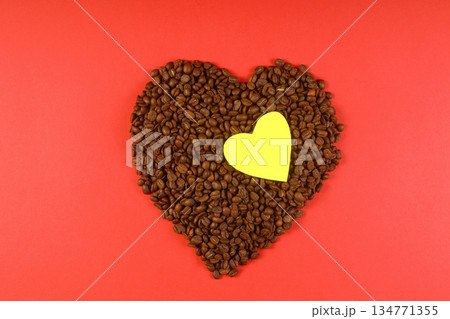 Heart coffee. Roasted coffee beans in the shape of heart on bright red background. Concept of coffee love, Valentines Day, good mood, gift. With yellow heart shape. Heart coffee. Roasted coffee beans in the shape of heart on bright red background. Concept of coffee love, Valentines Day, good mood, gift. With yellow heart shape. 134771355