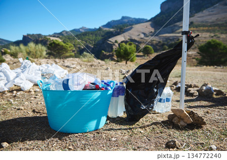 Outdoor Mountain Cleanup Scene With Blue Bucket Of Plastic Bottles And Bagged Waste Outdoor Mountain Cleanup Scene With Blue Bucket Of Plastic Bottles And Bagged Waste 134772240