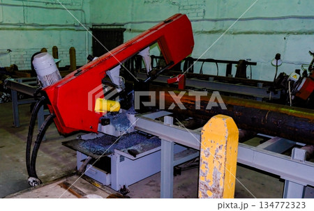 Industrial horizontal band saw cutting large steel pipe in workshop 134772323