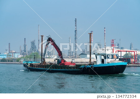 Work Barge with Crane Passing Industrial Refinery in Porto Marghera, Venice, Italy 134772334