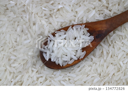 Raw white rice on wooden background. Long uncooked rice in wooden plate. Natural organic food. Traditional Asian cereal culture. 134772826