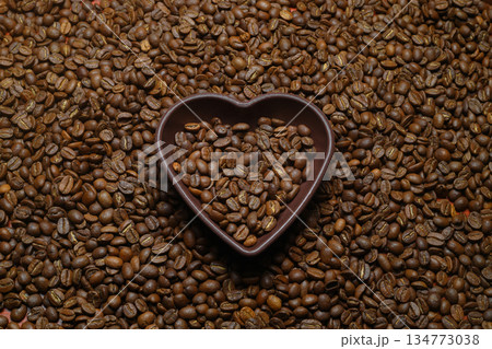 Roasted coffee beans in heart shaped bowl on coffee background. Love coffee concept. Roasted coffee beans in heart shaped bowl on coffee background. Love coffee concept. 134773038