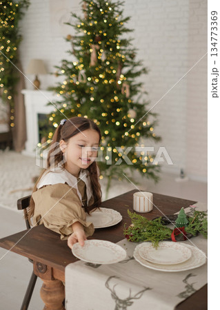 The girl helps the family to arrange the plates on the festive table on Christmas Eve. Preparing for the New Year celebration 134773369