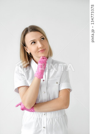 A thoughtful female doctor in pink gloves is thinking while looking away. A nurse on a white studio background 134773378