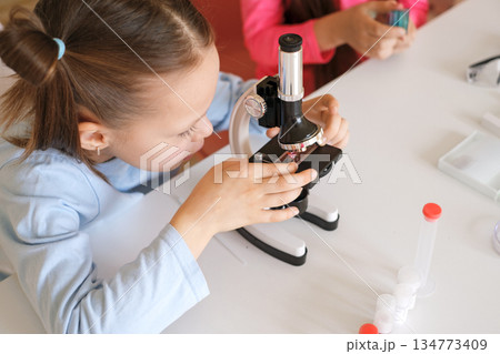 The girl puts the test tube under the magnifying glass of the microscope. Samples for observations and research of the microcosm The girl puts the test tube under the magnifying glass of the microscope. Samples for observations and research of the microcosm 134773409