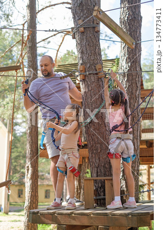 A father helps his daughter install a carabiner on the rope of a suspended rope amusement park. Rock climbing skills training A father helps his daughter install a carabiner on the rope of a suspended rope amusement park. Rock climbing skills training 134773411
