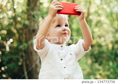 Young boy outdoors lifts a red tablet, capturing a bright moment of childhood Young boy outdoors lifts a red tablet, capturing a bright moment of childhood 134773756