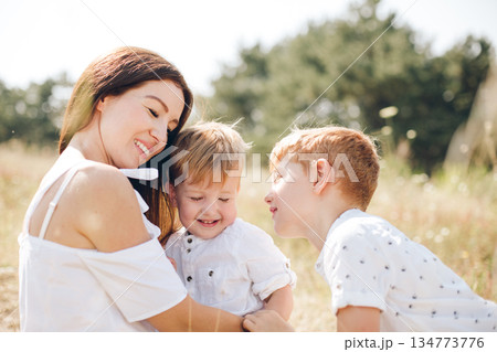 Mother and her two sons share a joyful moment in a sunlit outdoor field 134773776