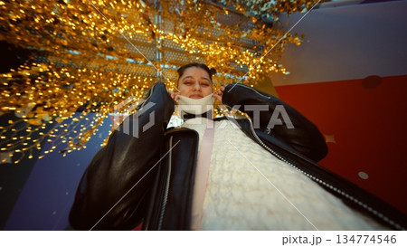 Woman smiles under shimmering fairy lights at evening celebration 134774546