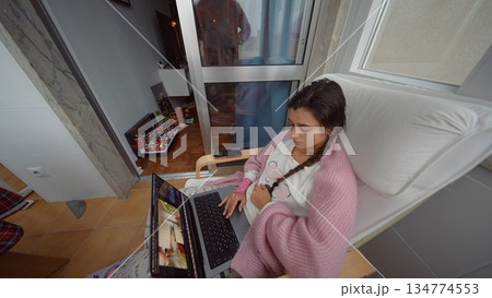 Lady in pink dress concentrates on image editing outside on balcony 134774553